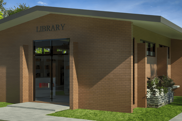 alt=’Exterior view of a brick library building with a glass entrance and landscaped flower beds'