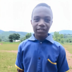 alt=’A young male student in a blue shirt poses outdoors, with a scenic backdrop of hills and greenery'